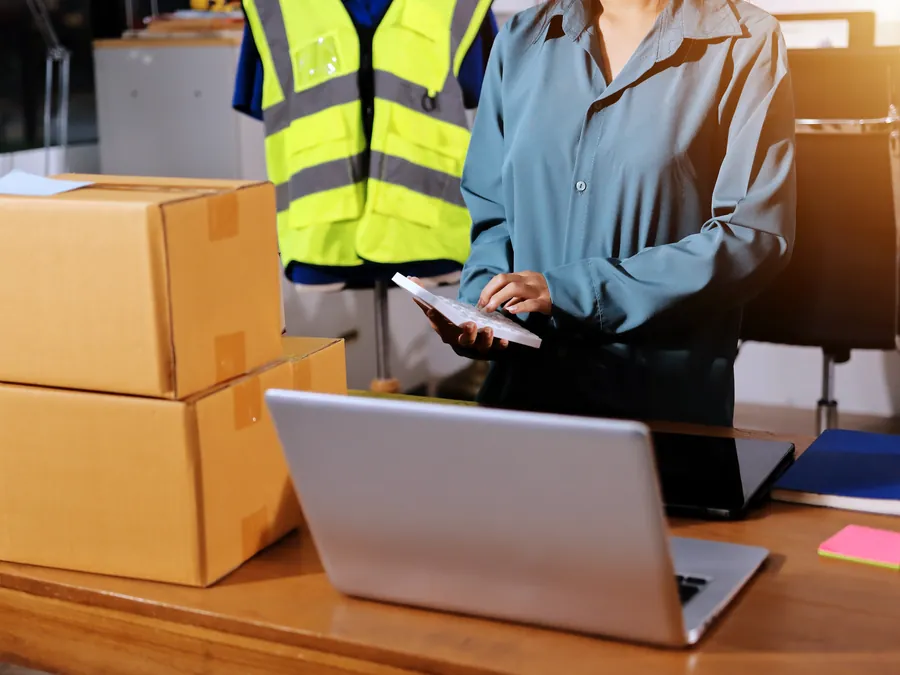 Warehouse office staff checking orders on a laptop next to parcels