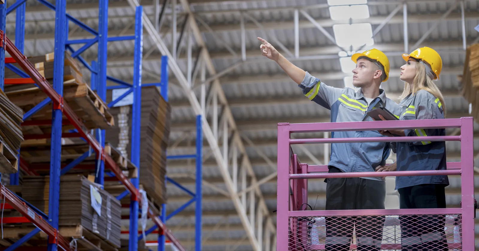 Two warehouse workers on a lift checking stock high on the racking