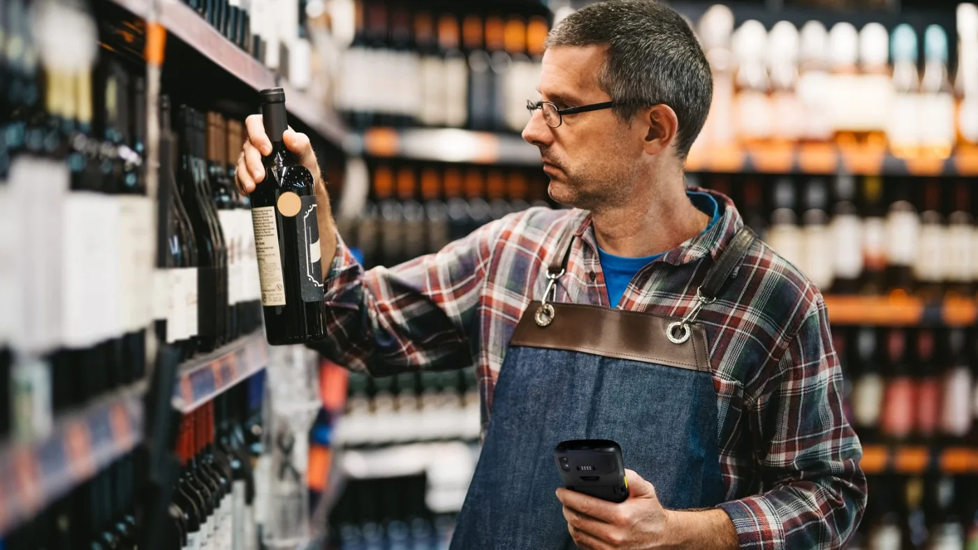 Employé de magasin vérifiant une bouteille de vin en rayon avec un terminal portable Zebra